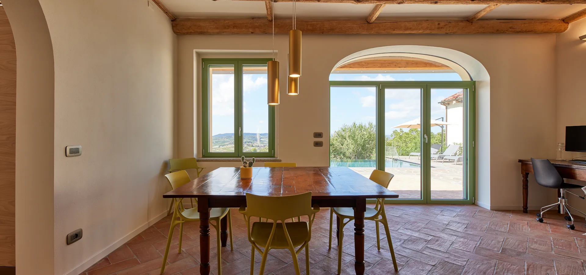 Villa Ozzano Monferrato - Zona pranzo del living con pavimenti in cotto fatto a mano, travi in legno originali restaurate, tavolo pranzo d'epoca a libro in legno e vista panoramica sulla piscina infinity e sulle colline del Monferrato - Design FSA Filippo Selis Architetto