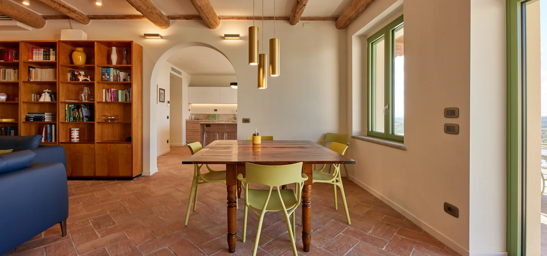 Villa Ozzano Monferrato - Zona pranzo del living con pavimenti in cotto fatto a mano, travi in legno originali restaurate, tavolo pranzo d'epoca a libro in legno e vista sulla cucina semiaperta - Design FSA Filippo Selis Architetto