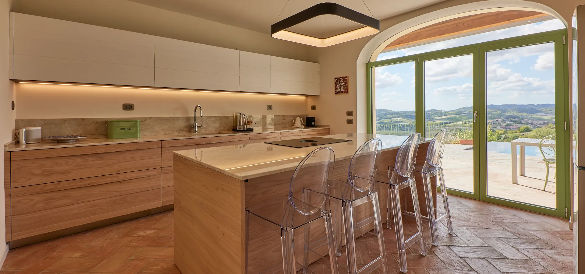 Villa Ozzano Monferrato - Isola con piano snack della cucina, realizzata artigianalmente su disegno originale in legno di olmo e quarzite naturale, con pavimento in cotto realizzato a mano e vista panoramica sulla piscina infinity - Design FSA Filippo Selis Architetto