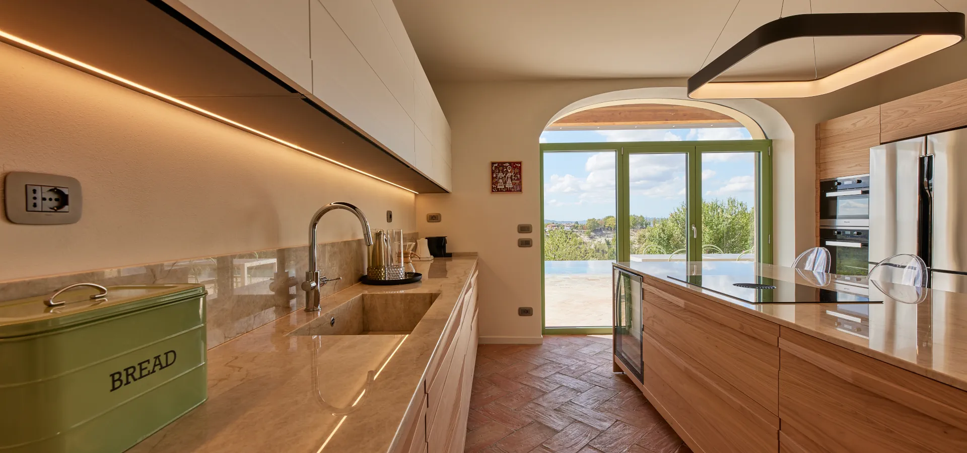 Villa Ozzano Monferrato - Vista della cucina, realizzata artigianalmente su disegno originale in legno di olmo e quarzite naturale, con pavimento in cotto realizzato a mano e vista sulla piscina infinity - Design FSA Filippo Selis Architetto